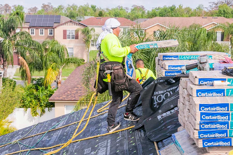 roofer in a flourescent shirt with a pile of roof materials