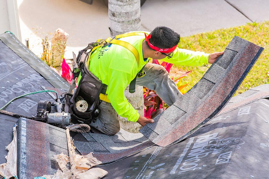 roofer with flourescent shirt installing asphalt roof